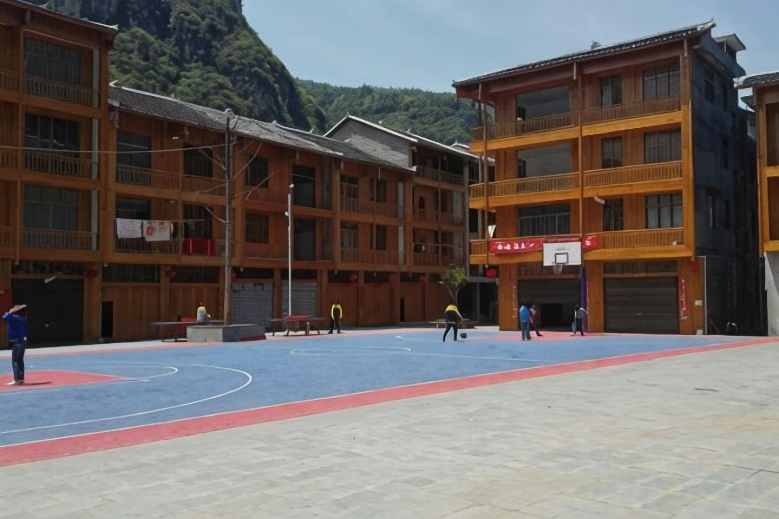Una cancha de baloncesto al aire libre rodeada de edificios de varios pisos con balcones, un aro de baloncesto y un cielo despejado.