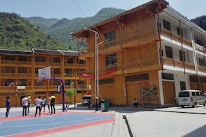 Un edificio de varios pisos con una cancha de baloncesto al frente, rodeado de montañas.
