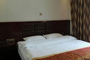 A hotel room with a large bed, a headboard, a nightstand, and a patterned curtain.