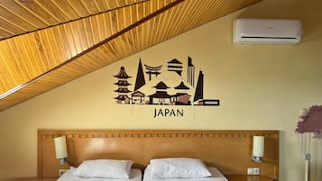 A hotel room with a wooden sloped ceiling, two beds with white bedding, a wall-mounted air conditioner, and a Japan-themed wall decal.