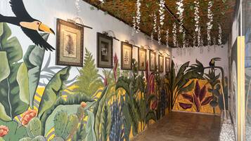 A hallway with a mural of tropical plants and birds, framed pictures on the wall, and hanging white flowers.