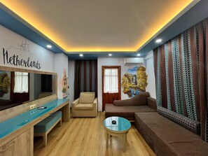 A living room with a wooden floor, a sofa, a chair, a coffee table, and a TV. - Esma Apart Hotel (Alanya)