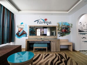 A living room with a TV, a sofa, a coffee table, and a wall with a mural. - Esma Apart Hotel (Alanya)