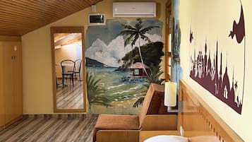 A hotel room with a bed, wooden furniture, a mural of a tropical beach scene, and a city skyline silhouette on the wall.