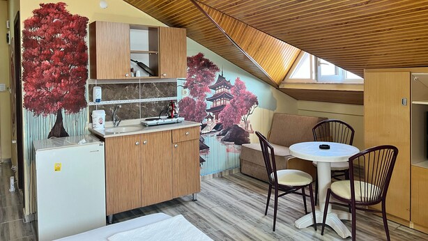 A compact kitchen with wooden cabinets, a sink, and a dining area with chairs. - Esma Apart Hotel (Alanya)