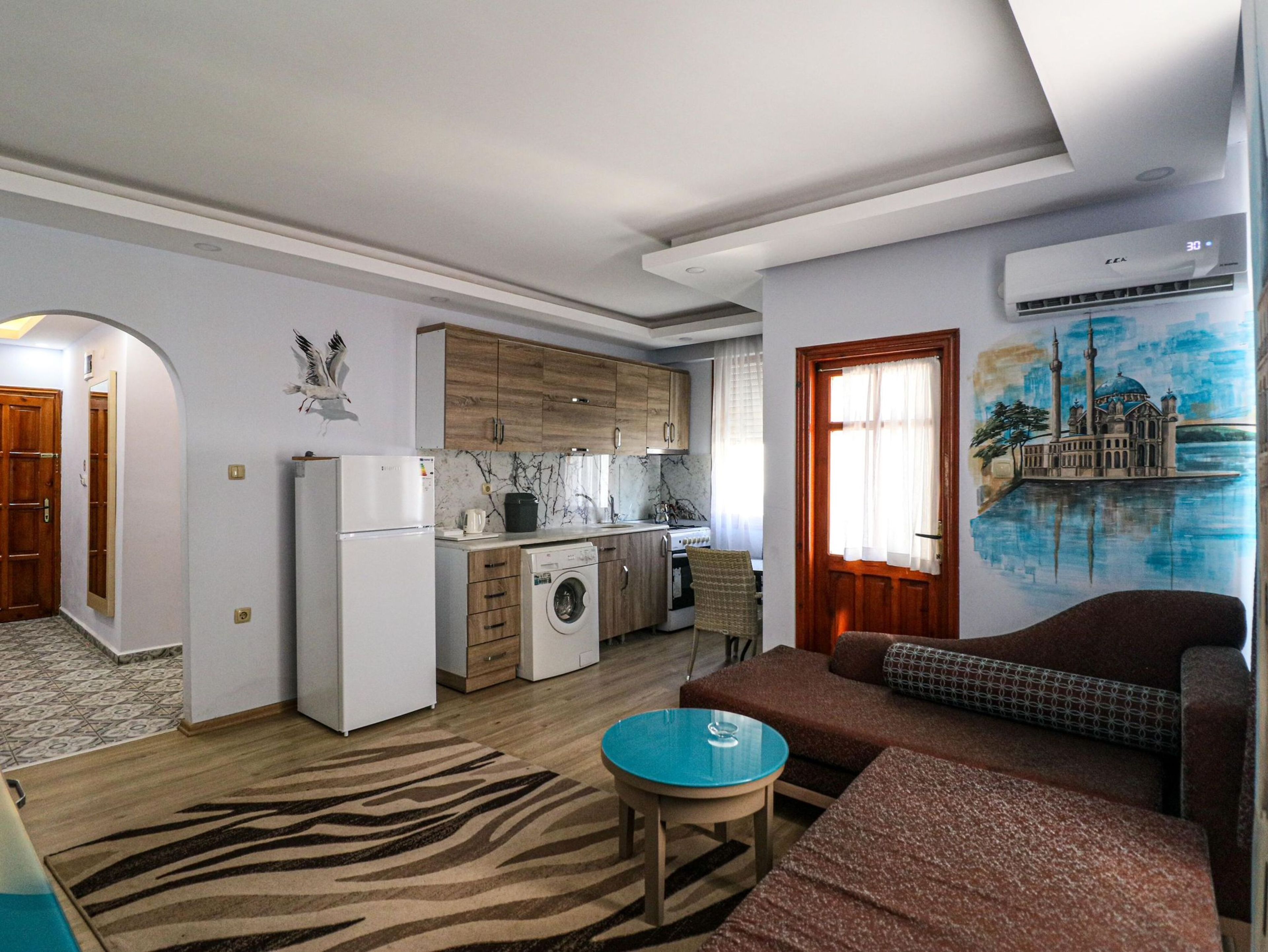 Un espacio habitable compacto con cocina, sofá, una mesita y un mural en la pared.