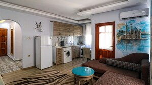 A compact living space with a kitchen, a sofa, a small table, and a mural on the wall. - Esma Apart Hotel (Alanya)