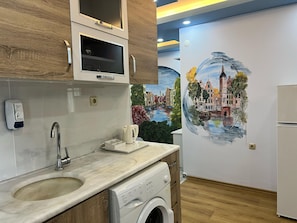 A modern kitchen with a built-in washing machine, a sink, and a coffee maker. - Esma Apart Hotel (Alanya)