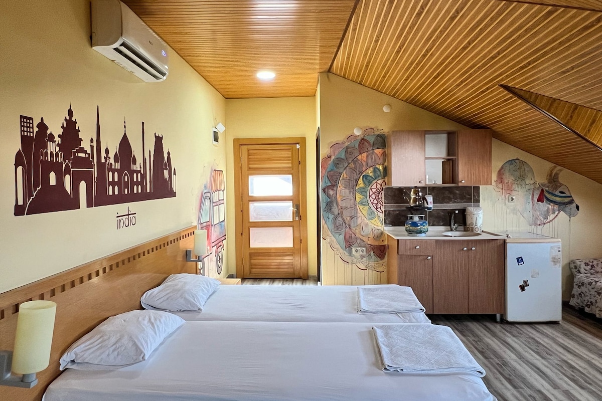 A hotel room with two beds, a kitchenette, and a mural of a cityscape.