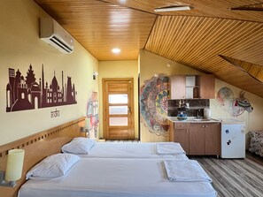 A hotel room with two beds, a kitchenette, and a mural of a cityscape. - Esma Apart Hotel (Alanya)