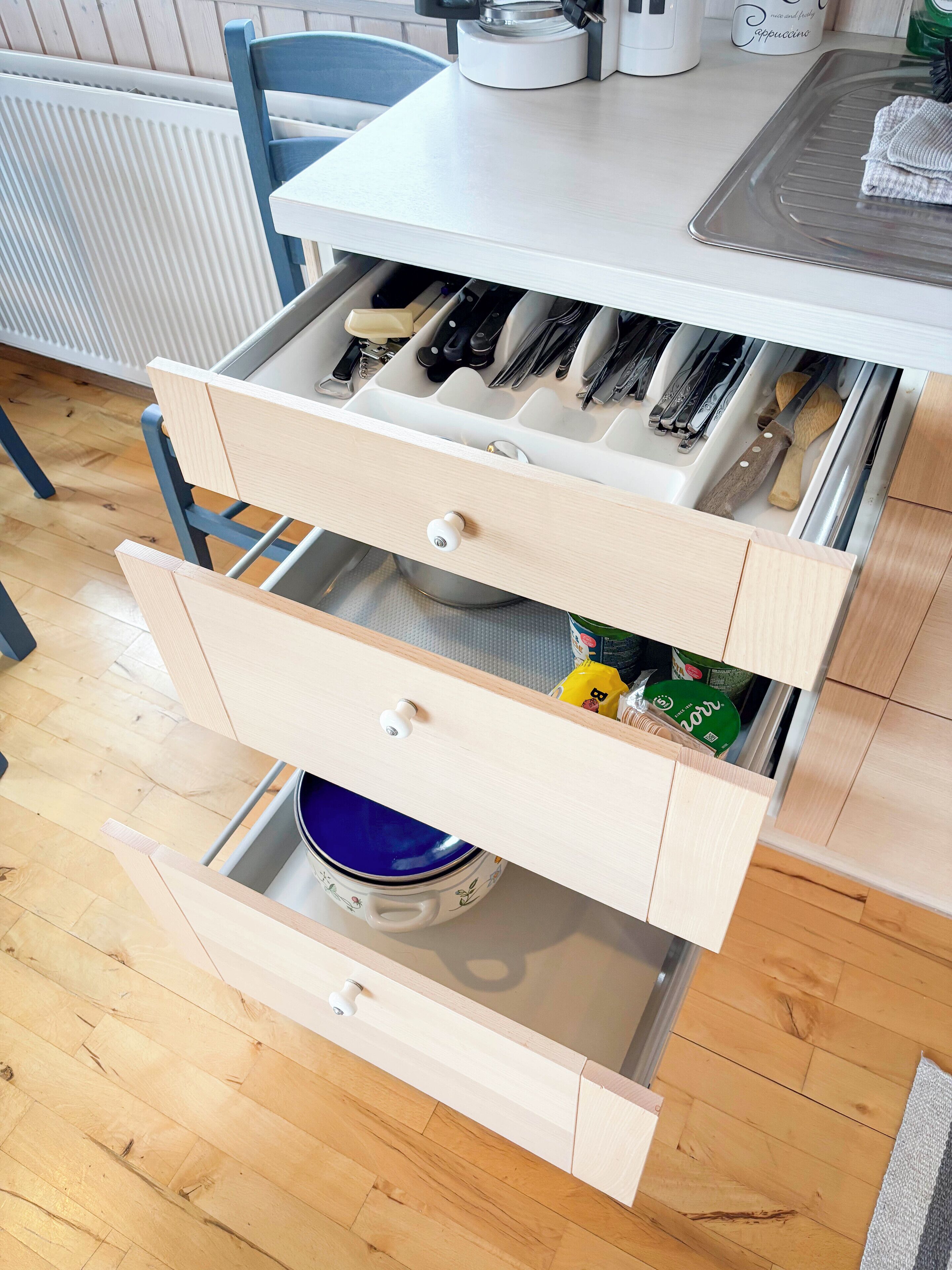 A kitchen with wooden cabinets, a white countertop, and a drawer organizer with utensils.