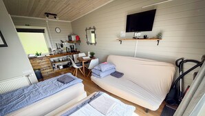 Una habitación compacta y bien iluminada, con dos camas individuales, un sofá, una pequeña mesa de comedor, un televisor montado en la pared y un aspirador.