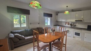 Een compacte keuken met witte kasten, een eettafel met stoelen, een bank en twee hanglampen.