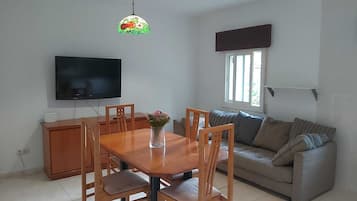 Een woonkamer met een houten eettafel, stoelen, een bank, een televisie en een raam.
