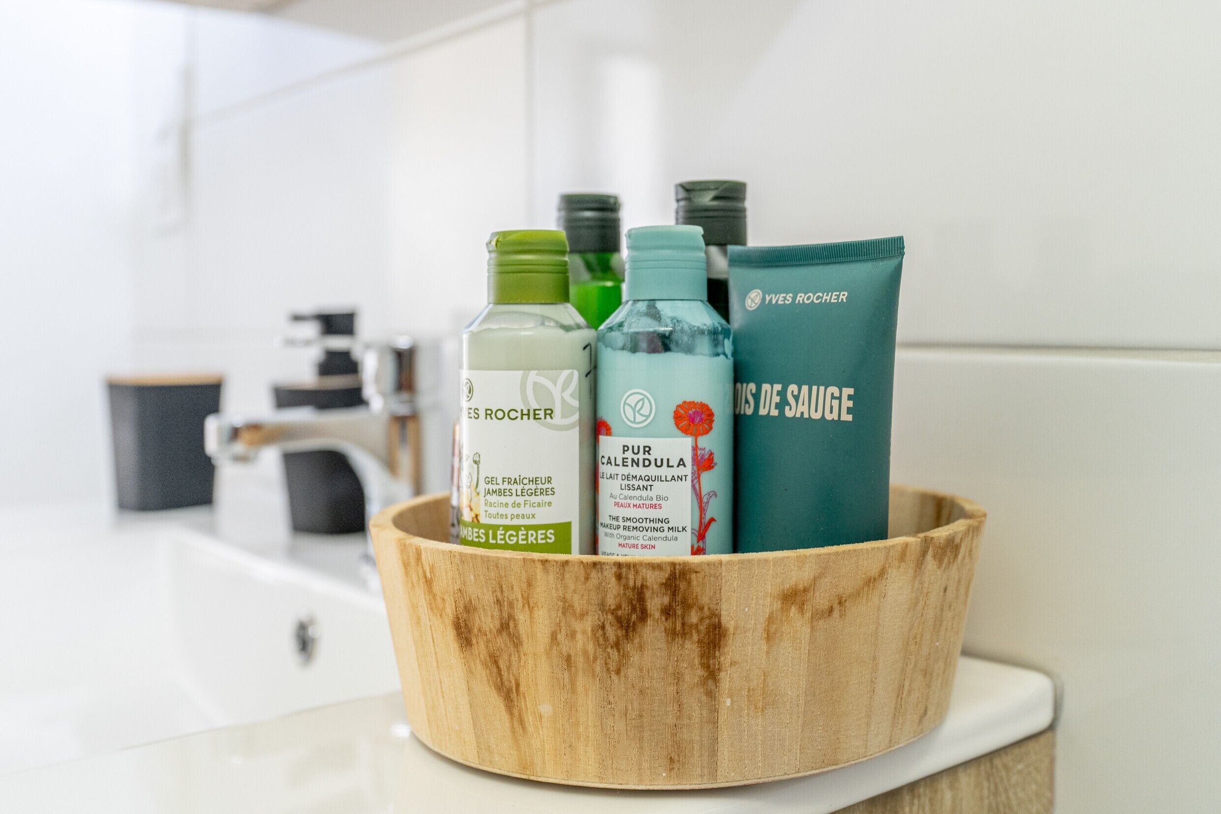 A wooden bowl containing skincare products on a white countertop.