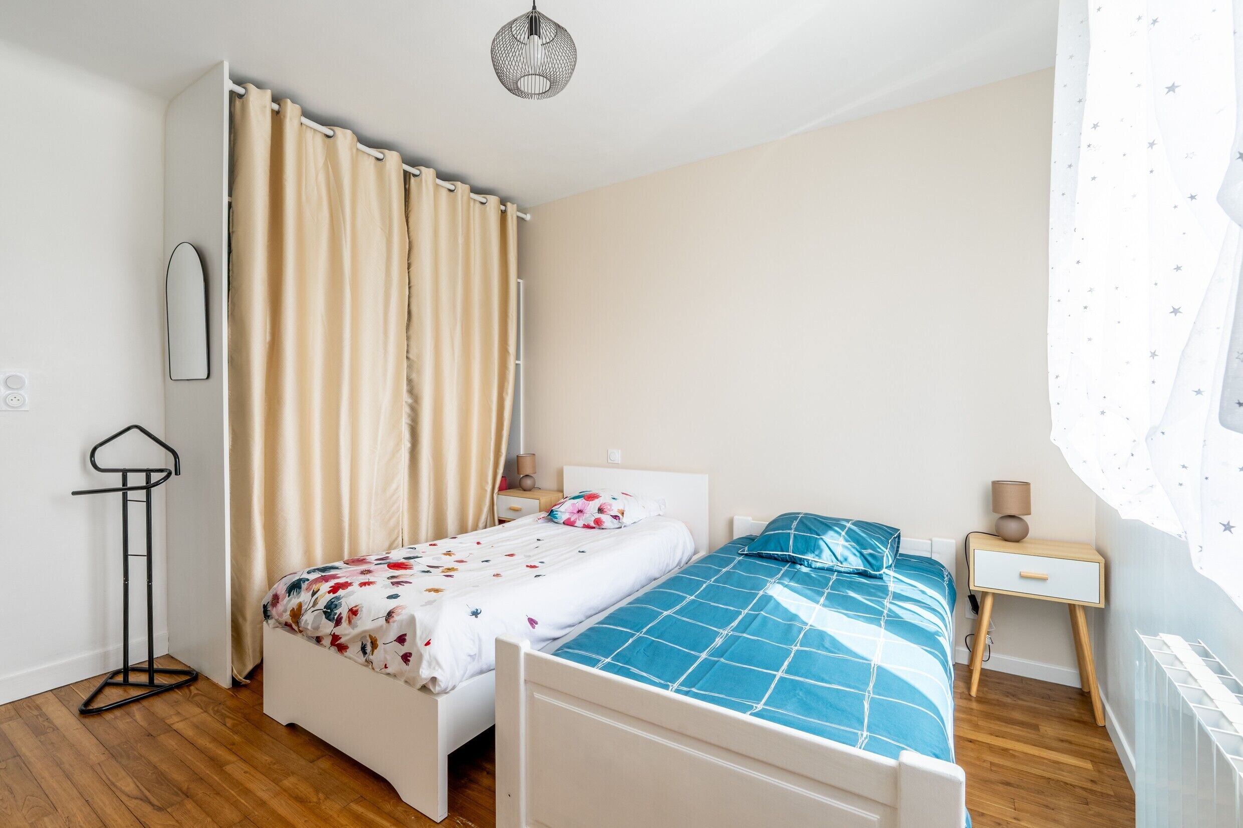 Un dormitorio con dos camas, una mesita de noche, una lámpara, un espejo y una lámpara colgante.