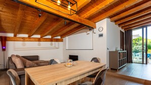 A dining area with a wooden table, chairs, a sofa, and a view through a glass door to an outdoor area. - Vanilla Bay Dep Apartment with Private Pool, Private Garden, and Air Conditioning (San Giovanni La Punta)