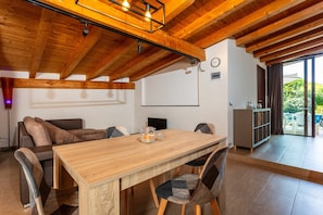 Un espace repas comprenant une table en bois, des chaises, un canapé et une vue sur l’extérieur, accessible par une porte vitrée.