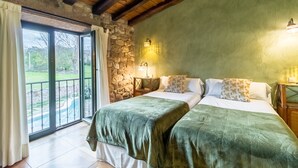 A room with two beds, a stone wall, a balcony with a view, and a wooden ceiling.