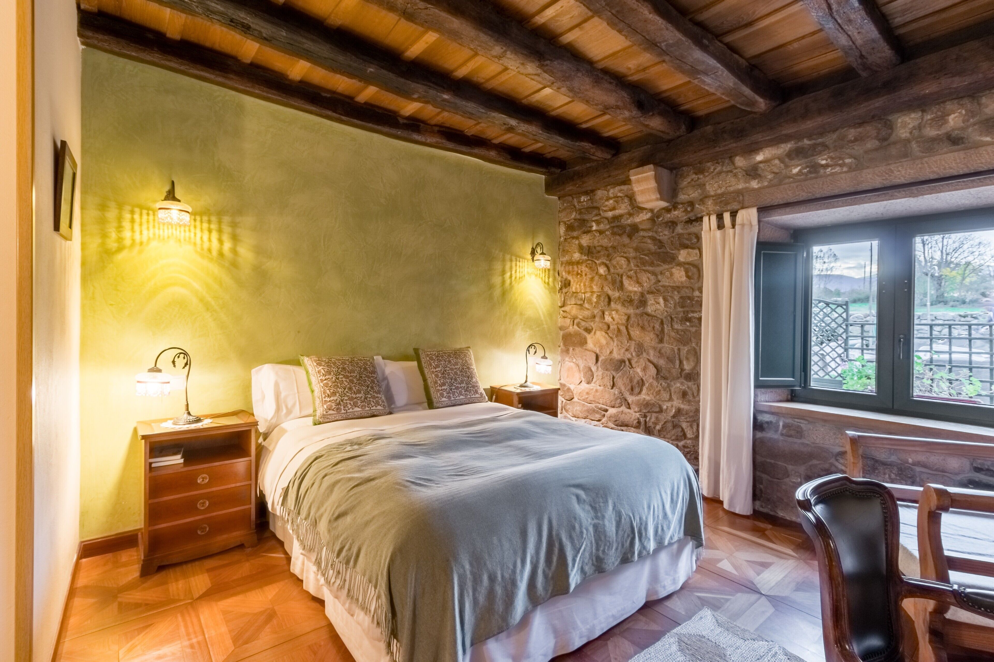 Una camera da letto con un letto, comodini in legno, una parete in pietra e una finestra con vista.