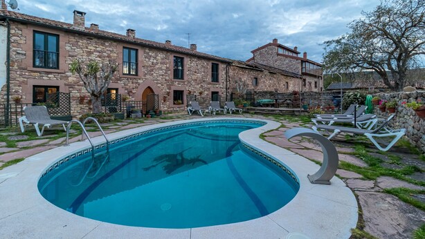 A stone building with a swimming pool, lounge chairs, and potted plants.