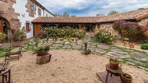 A courtyard with stone flooring, potted plants, and rustic wooden furniture.