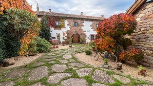A stone pathway leading to a rustic building with a tiled roof, surrounded by autumn foliage and potted plants.
