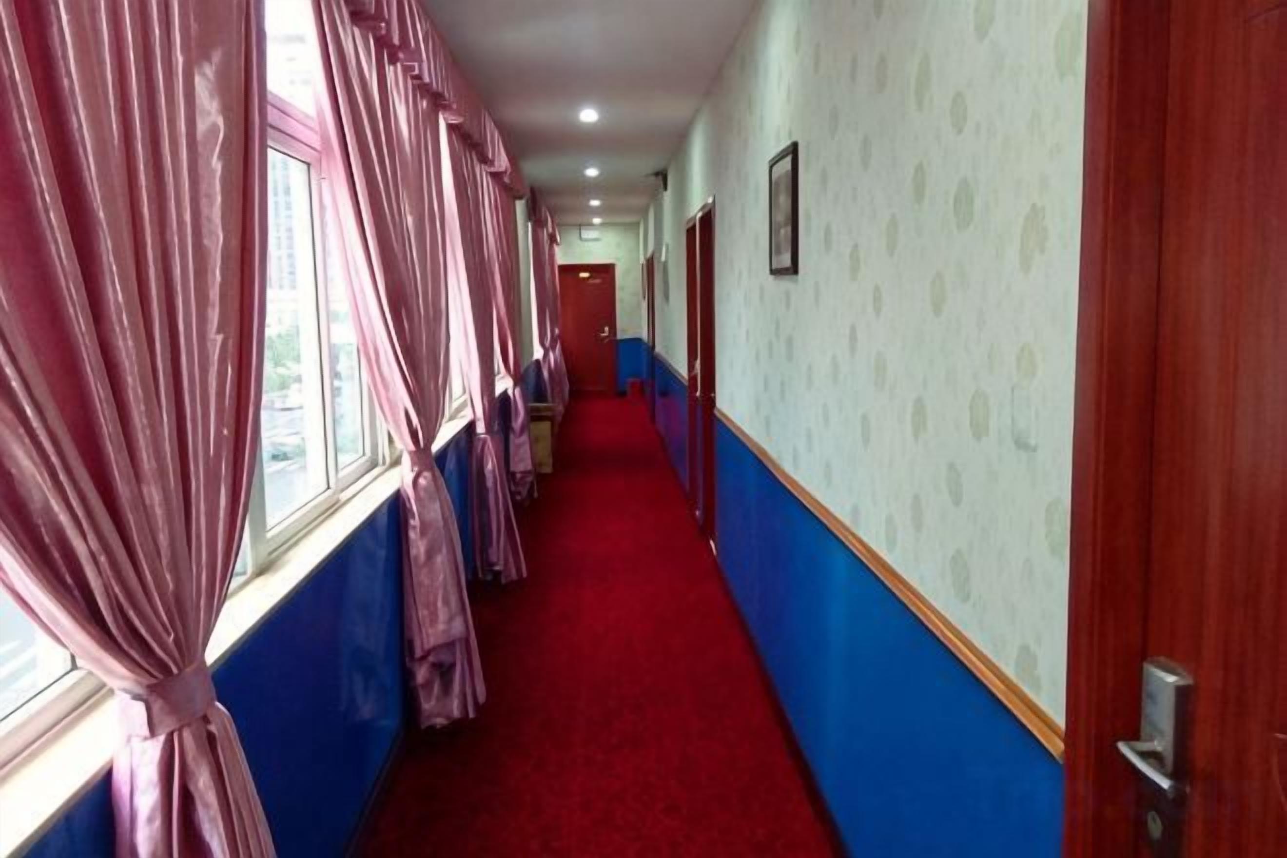 Un pasillo de hotel con alfombra roja, paredes azules y cortinas rosadas en las ventanas.