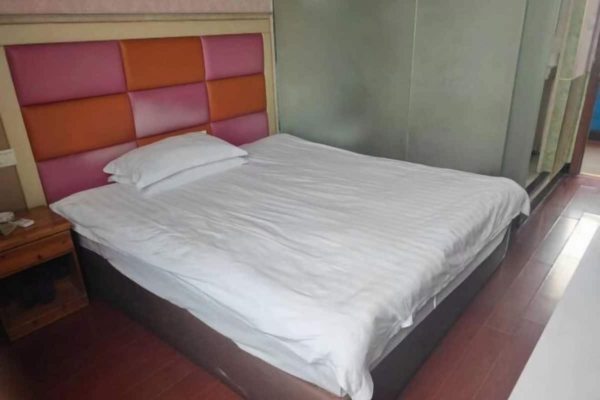 A single bed with a padded headboard, a wooden nightstand, and a plain wall.