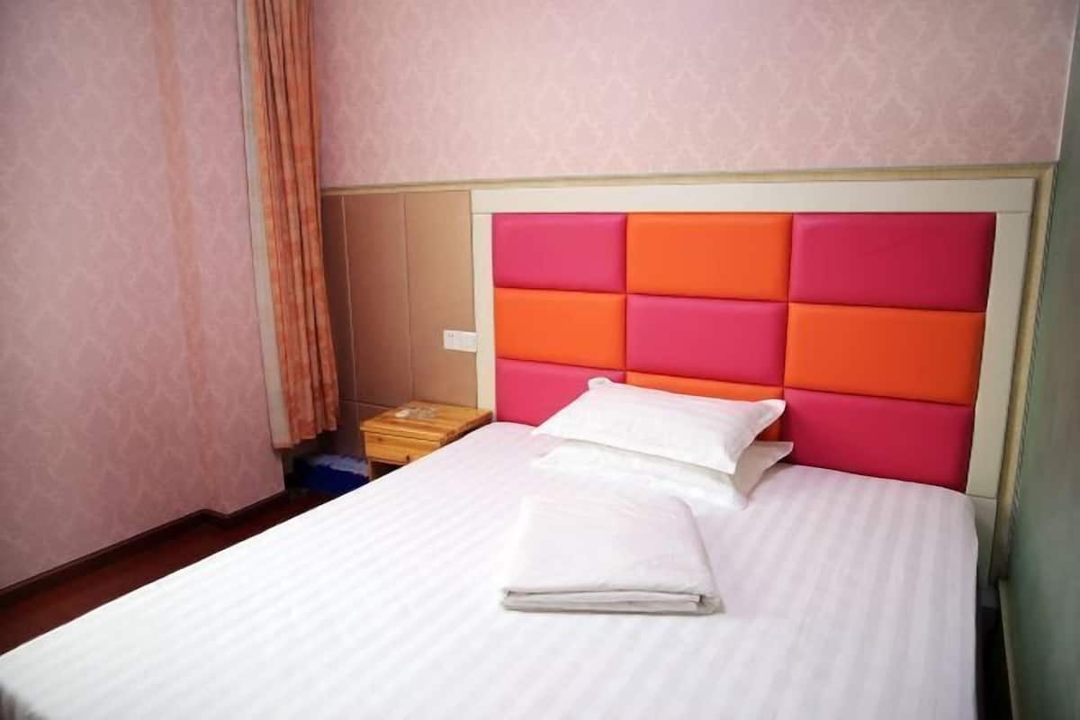 A neatly made bed with a white bedspread and pillows, a pink and orange headboard, and a wooden nightstand with a lamp.