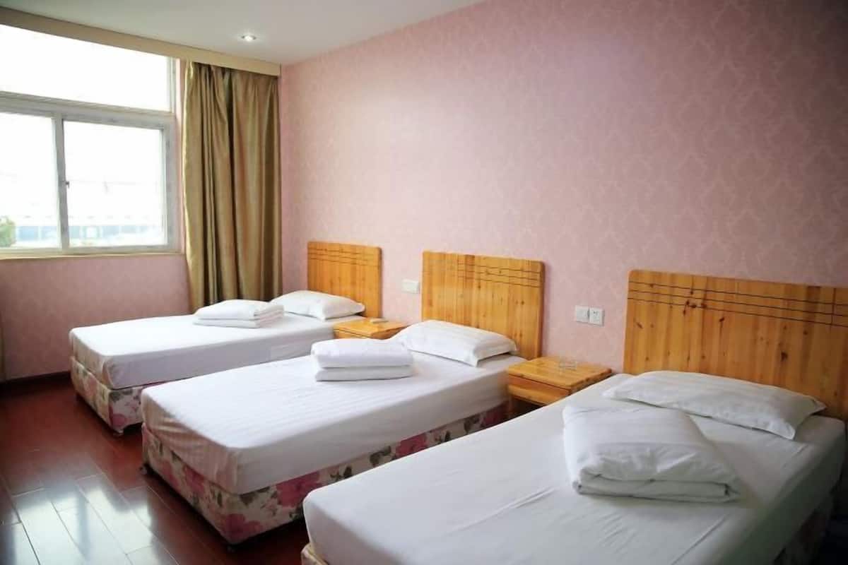 A hotel room with three single beds, wooden headboards, and a large window with curtains.