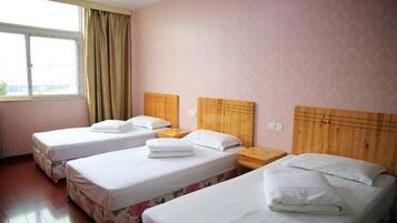 A hotel room with three single beds, wooden headboards, and a large window with curtains.