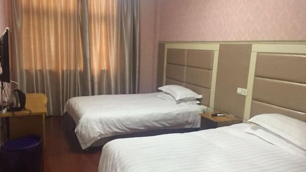 Une chambre d’hôtel avec deux lits simples, une table de chevet en bois, une poubelle et une fenêtre avec des rideaux.