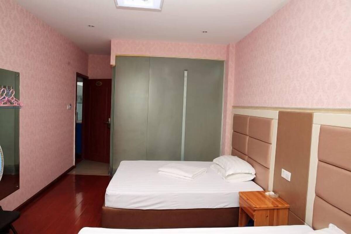 A hotel room with a bed, a wooden nightstand, a mirror, a wardrobe, and a door leading to another room.