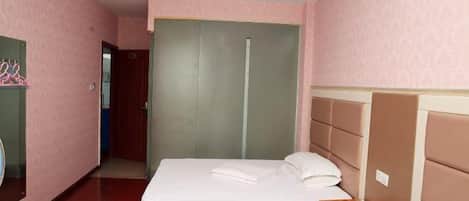 A hotel room with a bed, a wooden nightstand, a mirror, a wardrobe, and a door leading to another room.