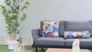 A grey sofa with floral cushions, a white vase, and a bamboo plant under a white umbrella. - Colorwave Terrace House (Matosinhos)