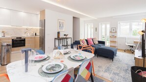 A modern living room with a sofa, a dining table set with plates and glasses, and a kitchen area with cabinets and appliances. - Colorwave Terrace House (Matosinhos)