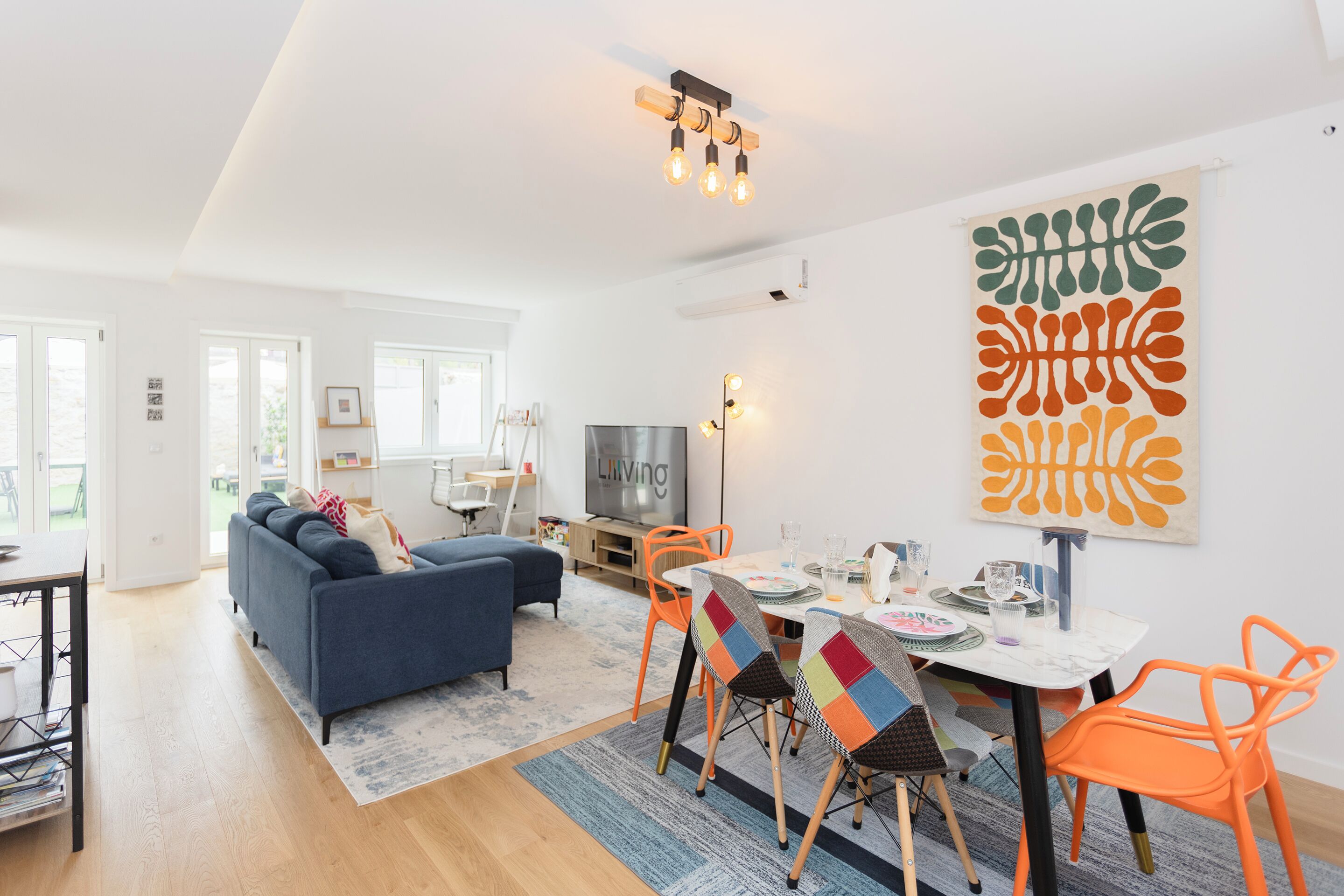 A modern living room with a sofa, dining table, chairs, and artwork on the wall.