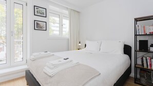 A modern hotel room with a large bed, a bookshelf, and a view through the window. - Colorwave Terrace House (Matosinhos)