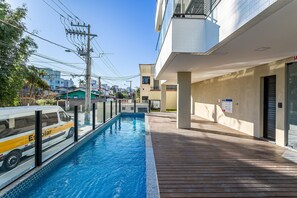 Une piscine située à côté d’un bâtiment doté d’un toit plat et d’une terrasse en bois.