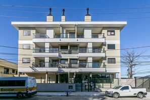 Un immeuble à plusieurs étages doté de balcons, d’une entrée sécurisée et d’un camionnette blanche garée devant.