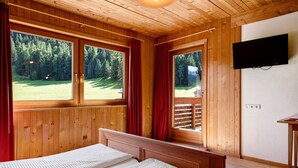 A wooden-paneled room with a bed, large windows, and a mounted TV.