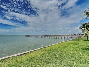 A waterfront view with a grassy area and a pier extending into the water. - Copano Coastal Gem by Miss Kitty’s (Rockport)