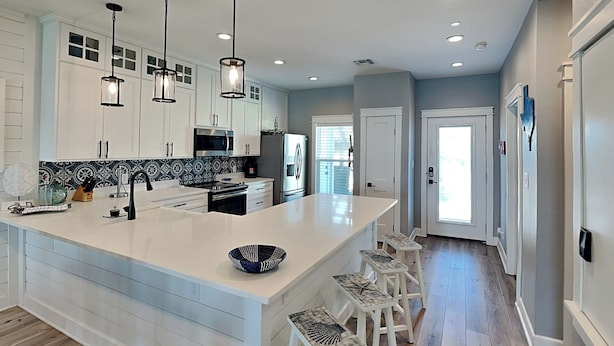 A modern kitchen with white cabinetry, a large island, bar stools, and pendant lighting. - Copano Coastal Gem by Miss Kitty’s (Rockport)