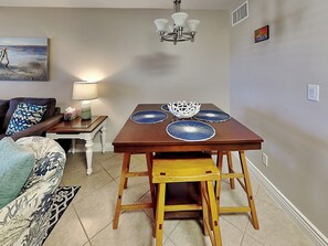 A dining area with a wooden table, blue placemats, and a white decorative bowl. - Kontiki Beach Resort #317 by Miss Kitty’s (Rockport)