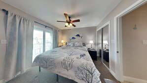 A bedroom with a bed, two bedside tables, a ceiling fan, and a view through a window. - Kontiki Beach Resort #317 by Miss Kitty’s (Rockport)