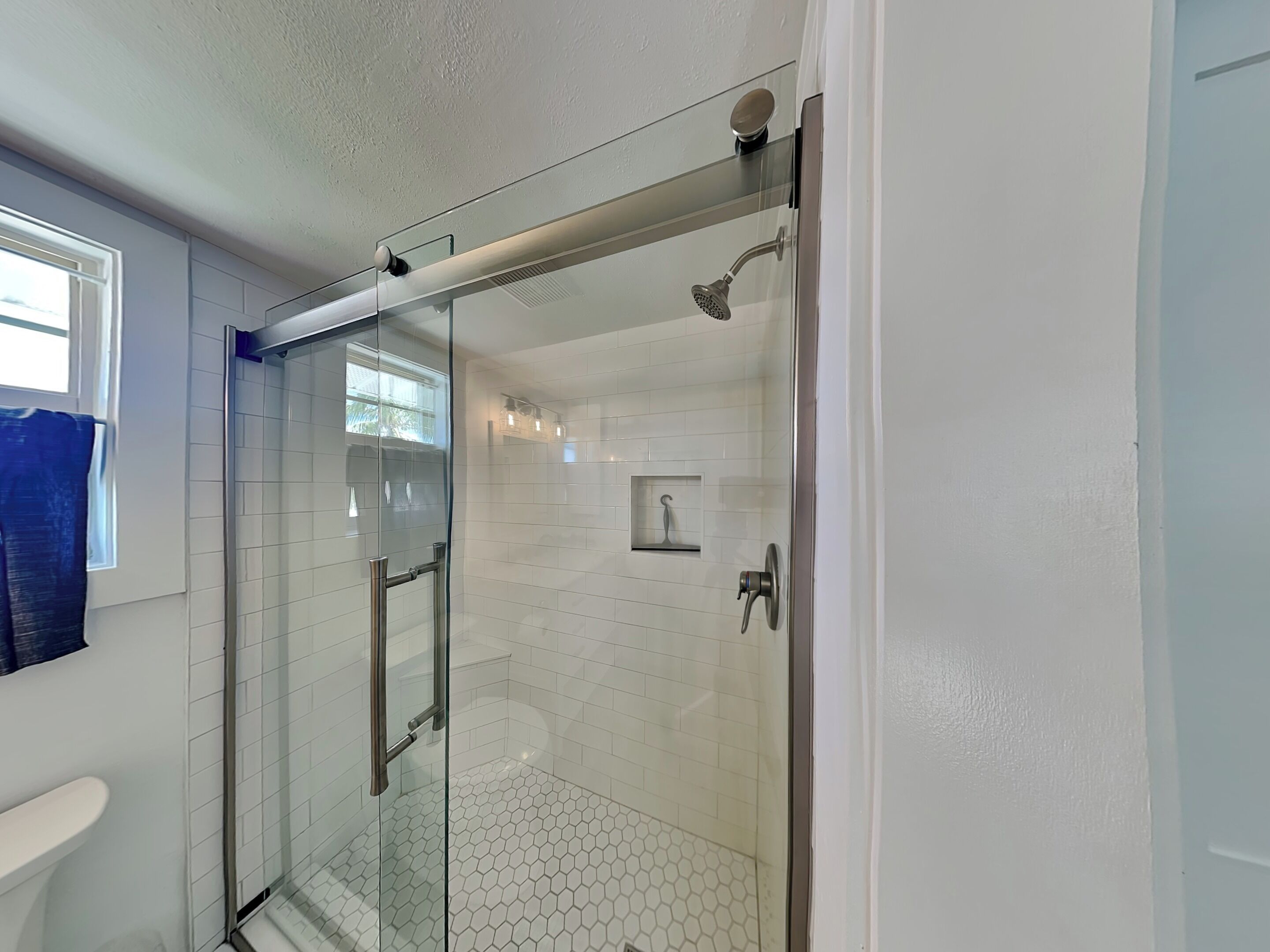 A modern bathroom with a glass-enclosed shower, white hexagonal tiles, and a visible towel rack.