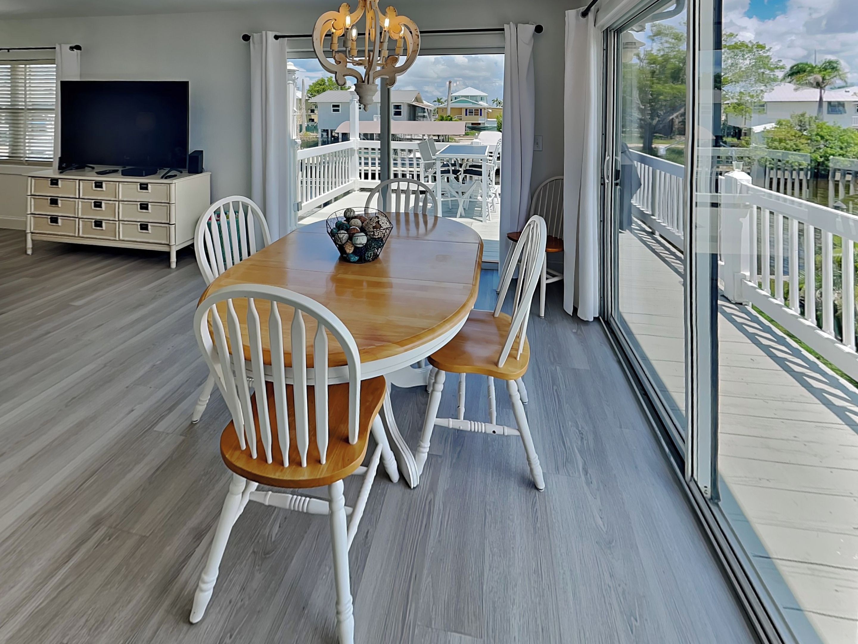 A dining area with a wooden table and white chairs, a TV on a cabinet, and a view of the outside.