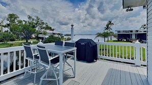 A deck with a table and chairs, a grill, and a view of the water and buildings. - 275 Blue Bay by Distinctive Beach Rentals (Fort Myers Beach)