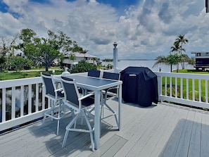 An outdoor deck with a table and chairs, a grill, and a view of the water and surrounding greenery.